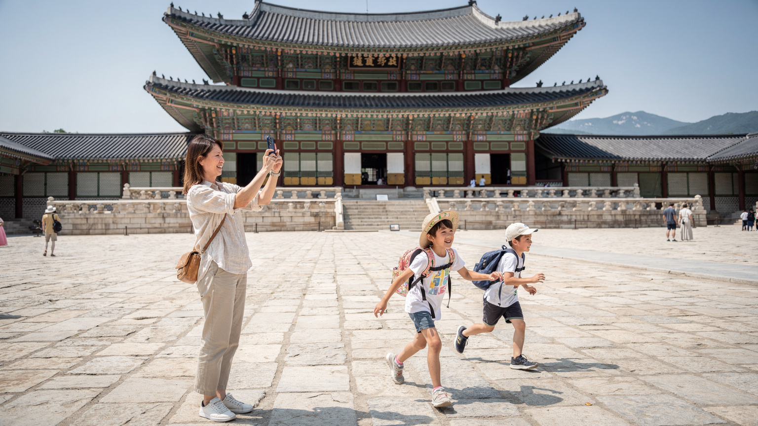 ソウルの景福宮の広場で、母親が携帯電話で写真を撮り、子供たちが後ろで遊んでいる様子。