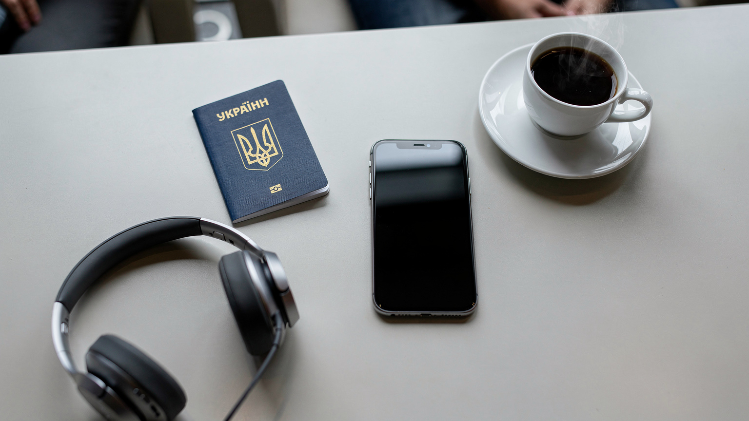 Охайний плоский знімок на столі в аеропорту: паспорт з українським тризубом, смартфон, навушники та чашка кави, що символізує подорож.