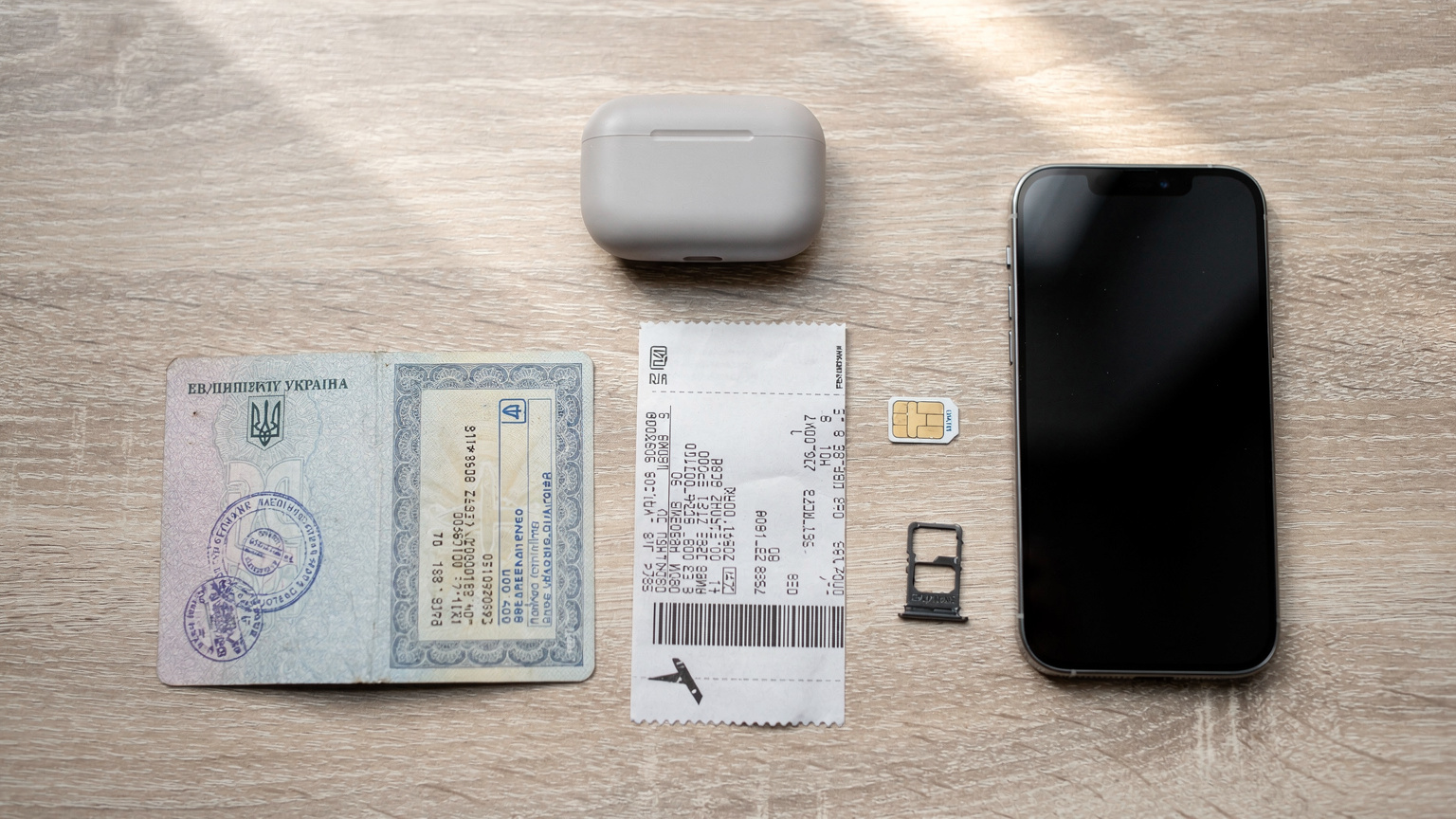Огляд столу з паспортом, авіаквитками, навушниками та iPhone 17 Pro Max, що лежить поруч з фізичною SIM-карткою.