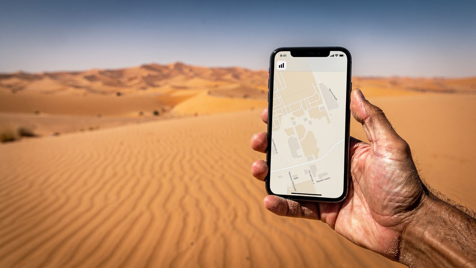 Ręka trzymająca smartfon z widoczną ikoną zasięgu, z rozległymi wydmami Sahary w tle.