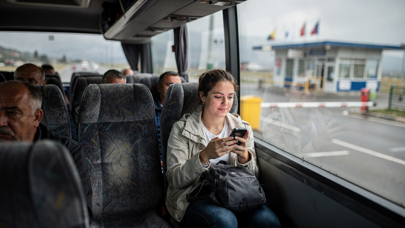 Ein überfüllter Bus, der sich einer Grenzkontrolle zwischen zwei Balkanländern nähert, während eine Reisende in ihrem Sitz entspannt auf ihr Smartphone schaut, ohne die Sorge um Netzverbindung.
