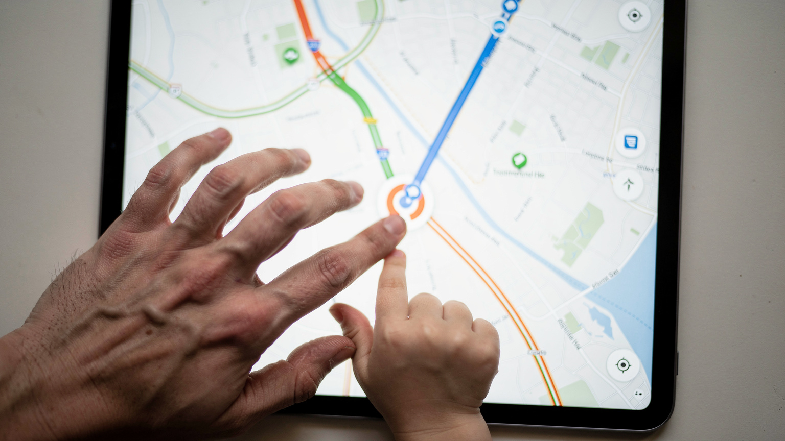 Close-up of a parent's hand gently guiding a child's finger on a tablet screen, showing a map application with a route highlighted.