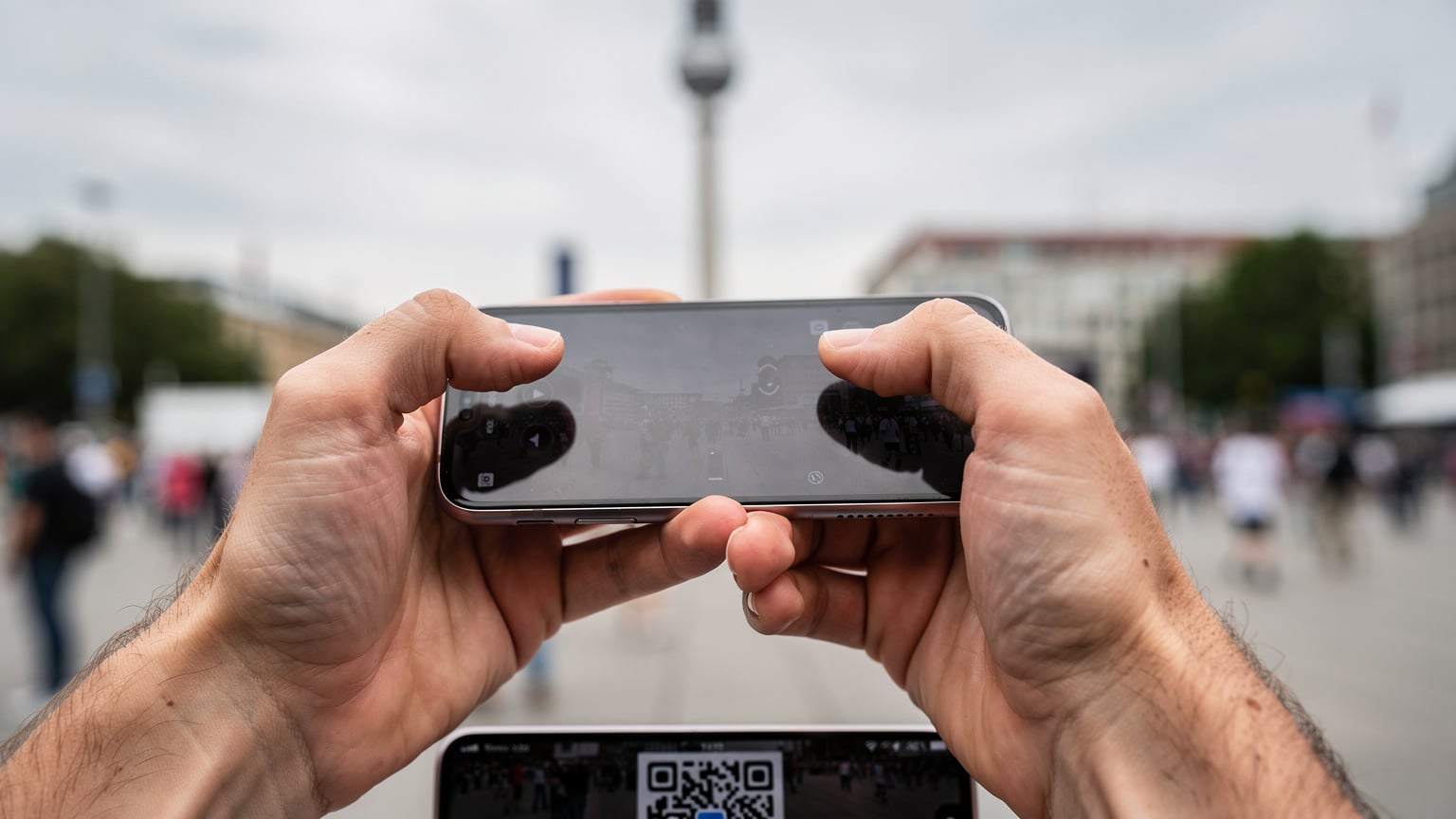 Nahaufnahme eines Smartphones in den Händen eines Reisenden, der gerade einen QR-Code scannt, um eine eSIM zu aktivieren, mit dem belebten Alexanderplatz im unscharfen Hintergrund.