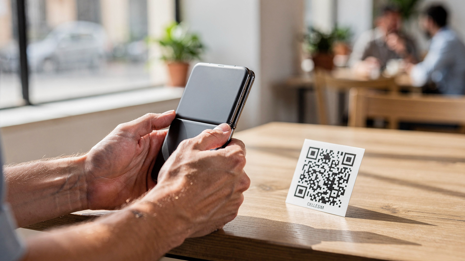 Unas manos humanas sosteniendo un Samsung Galaxy Z Flip 8 en un café moderno y luminoso en el barrio de Malasaña, Madrid, con un código QR de Cellesim sobre la mesa, indicando la facilidad de activación de la eSIM.