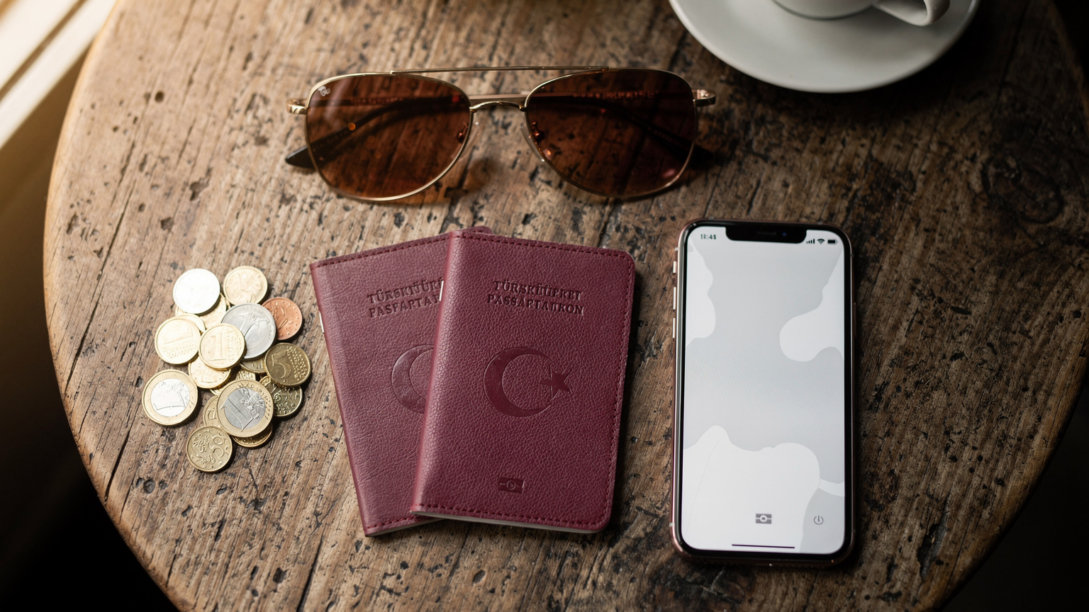 Bir kafeteryada oturmuş, seyahat planlarını ve eSIM seçeneklerini karşılaştıran bir gezginin üzerinde pasaportlar, bir telefon ve çeşitli para birimleri yer alıyor.