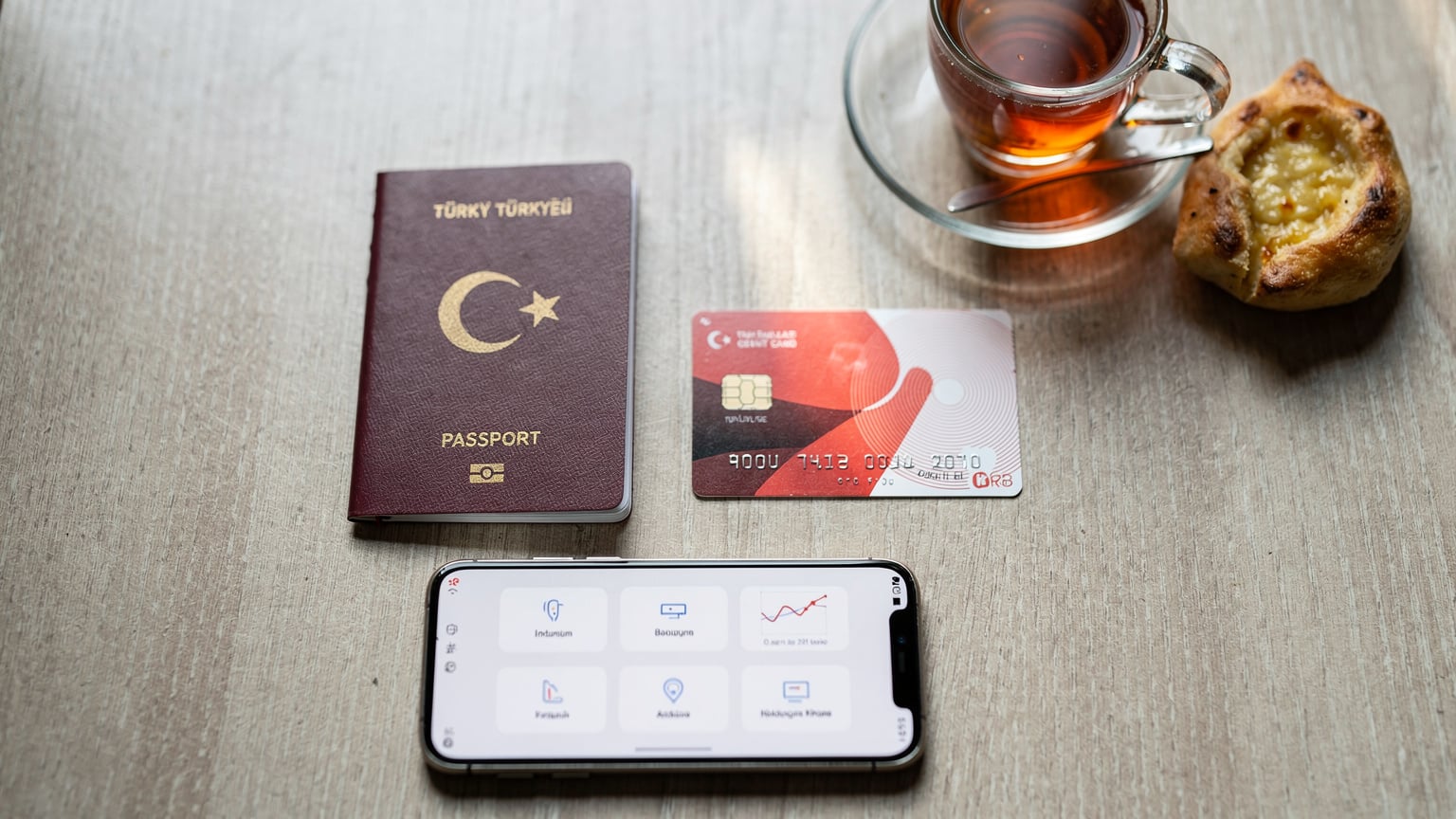 Tiflis'te bir kafe masasında, bir gezginin pasaportu, Türk banka kartı ve telefonu görülüyor, bankacılık uygulaması açık.