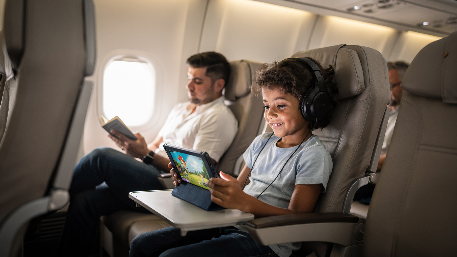 Criança brasileira de cerca de 6 anos com fones de ouvido, assistindo a um desenho animado em um tablet no assento do avião, com os pais lendo ao lado em um ambiente tranquilo.