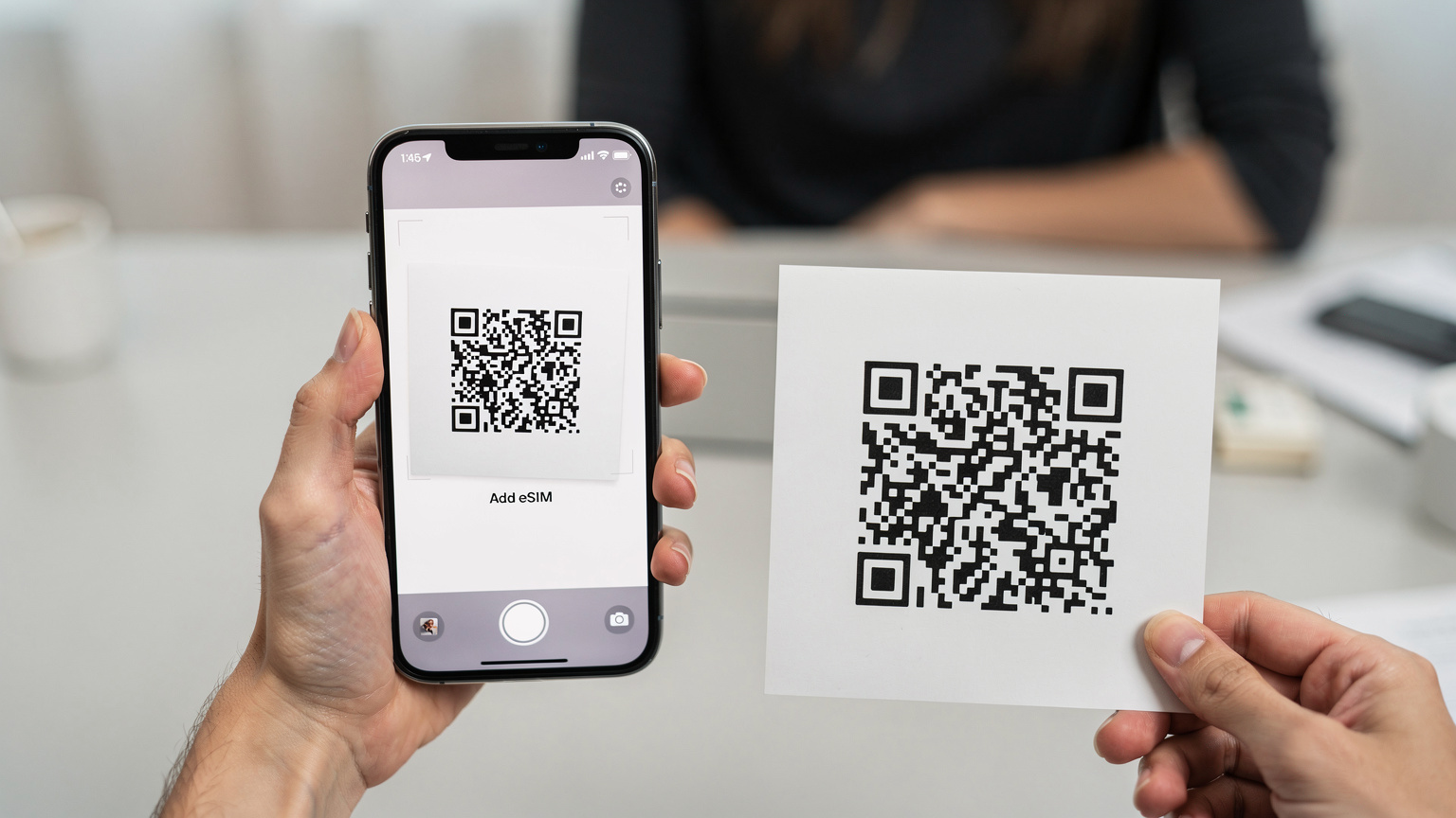Une main tenant un iPhone 17, l'écran affichant l'interface d'ajout d'eSIM avec l'appareil photo activé, prête à scanner un code QR imprimé sur une feuille de papier.
