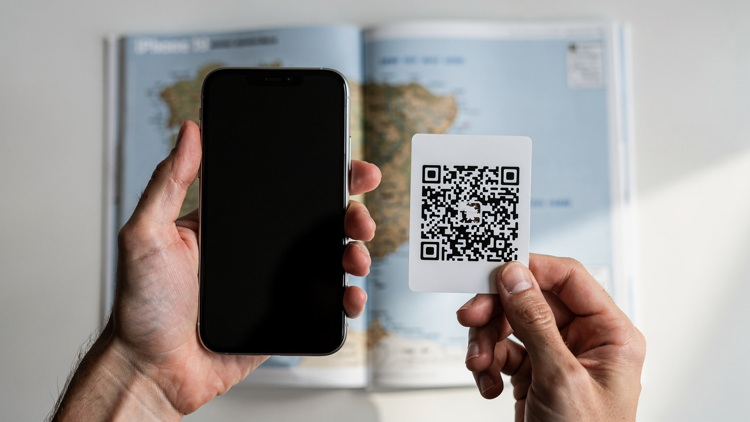As mãos de um viajante, segurando um iPhone 19 e um código QR de eSIM, prestes a digitalizá-lo para ativar um novo plano de dados, com um mapa de Portugal desfocado ao fundo.