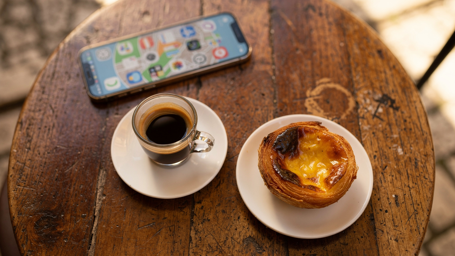 Uma mesa de café em Lisboa, com um copo de 'bica' e um pastel de nata, com um smartphone mostrando a tela do aplicativo Cellesim em segundo plano, sugerindo conectividade para desfrutar da cultura local.