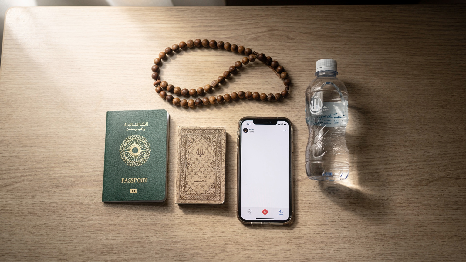 Pandangan atas sebuah flat-lay seorang jemaah haji yang sedang mengatur barangan perjalanannya, termasuk pasport Malaysia, telefon pintar dengan ikon eSIM, tasbih, buku doa kecil, dan sebotol air zam-zam mini, di sebuah meja hotel di Madinah.