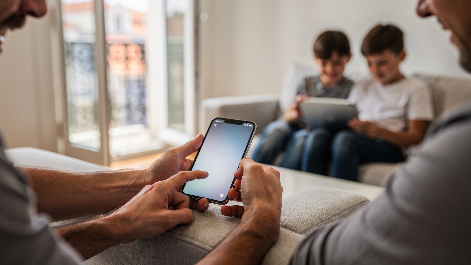 Des mains d'adultes configurant une eSIM sur un smartphone, tandis que des enfants jouent avec une tablette à l'arrière-plan dans un salon lumineux à Lisbonne.