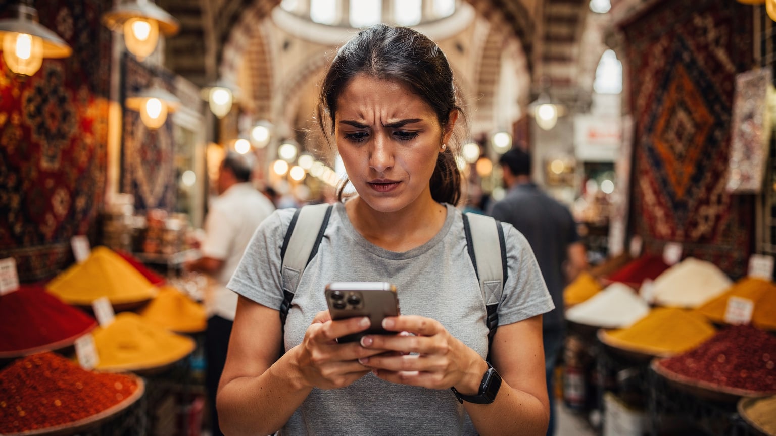 Een reiziger kijkt bezorgd naar haar smartphone in een drukke, chaotische bazaar in Istanbul, wijzend op potentiële connectiviteitsproblemen.