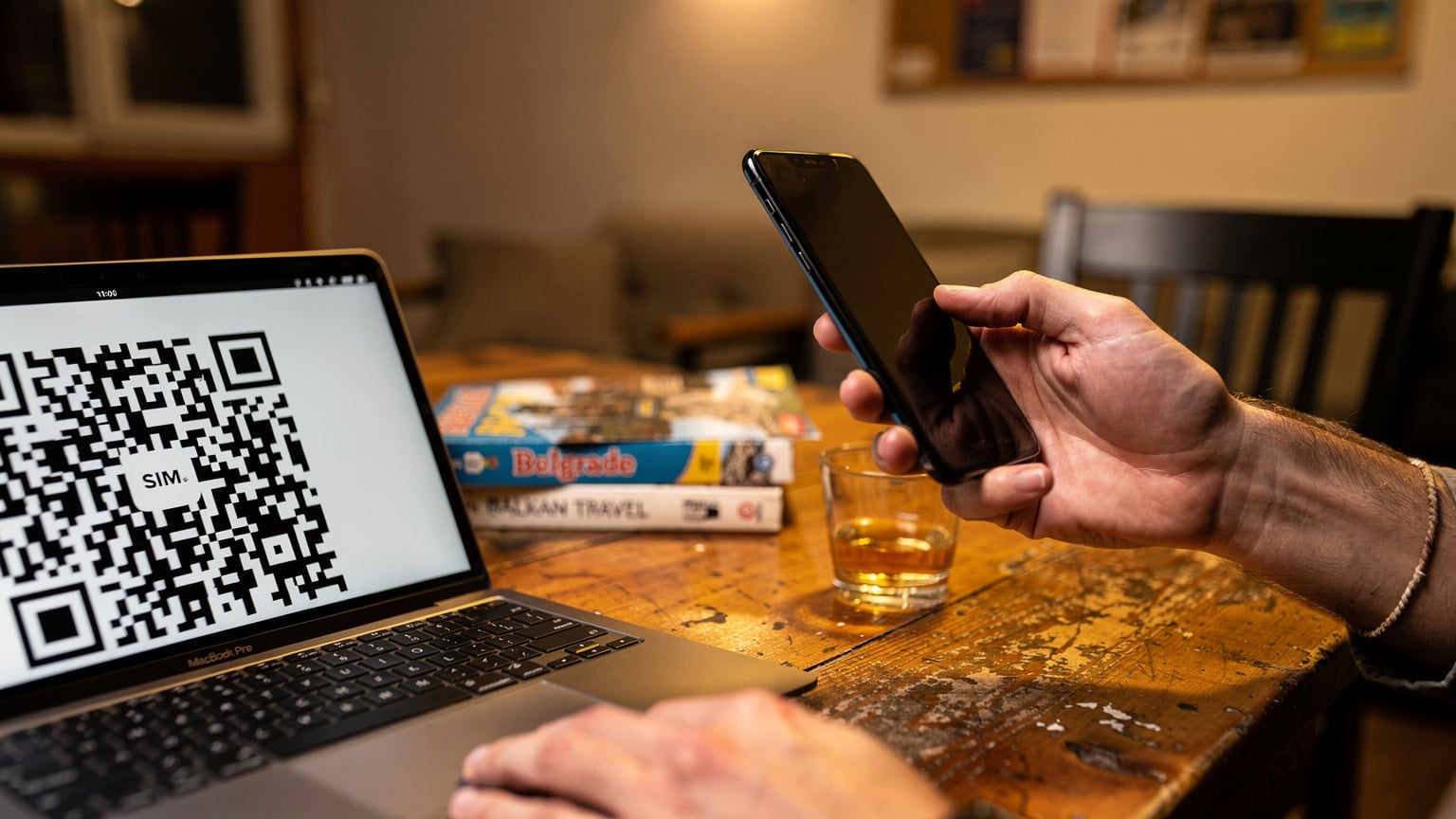 O mână ține un telefon modern, afișând un cod QR pe ecranul unui alt dispozitiv, în timpul procesului de configurare a unui eSIM într-un hostel din Belgrad.