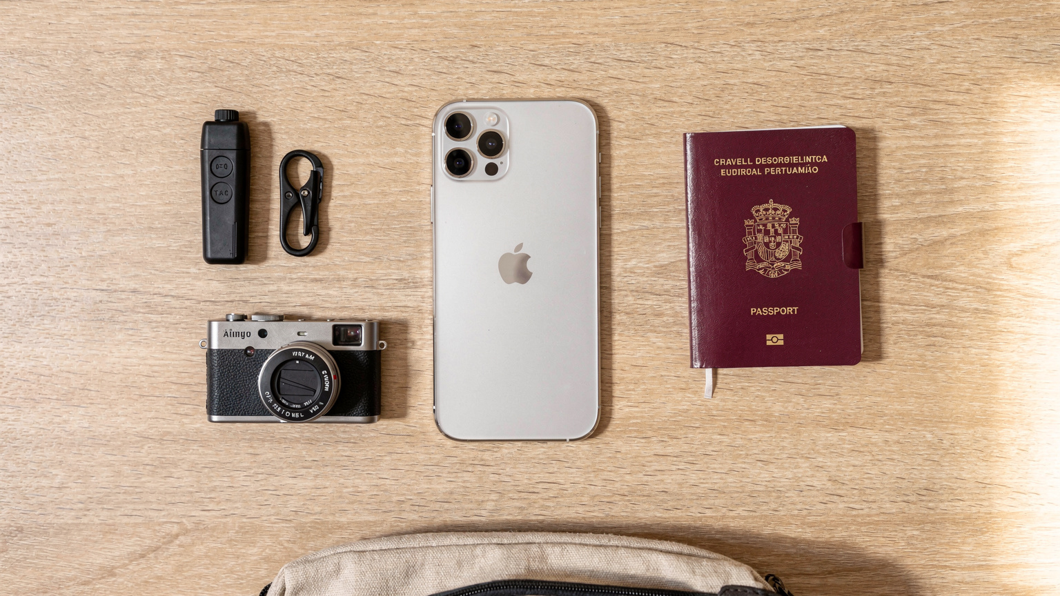 Uma vista aérea de um conjunto de itens essenciais para viagem dispostos sobre uma mesa: um iPhone 18, passaporte português, fones de ouvido sem fio e um pequeno mapa estilizado da Costa Vicentina.