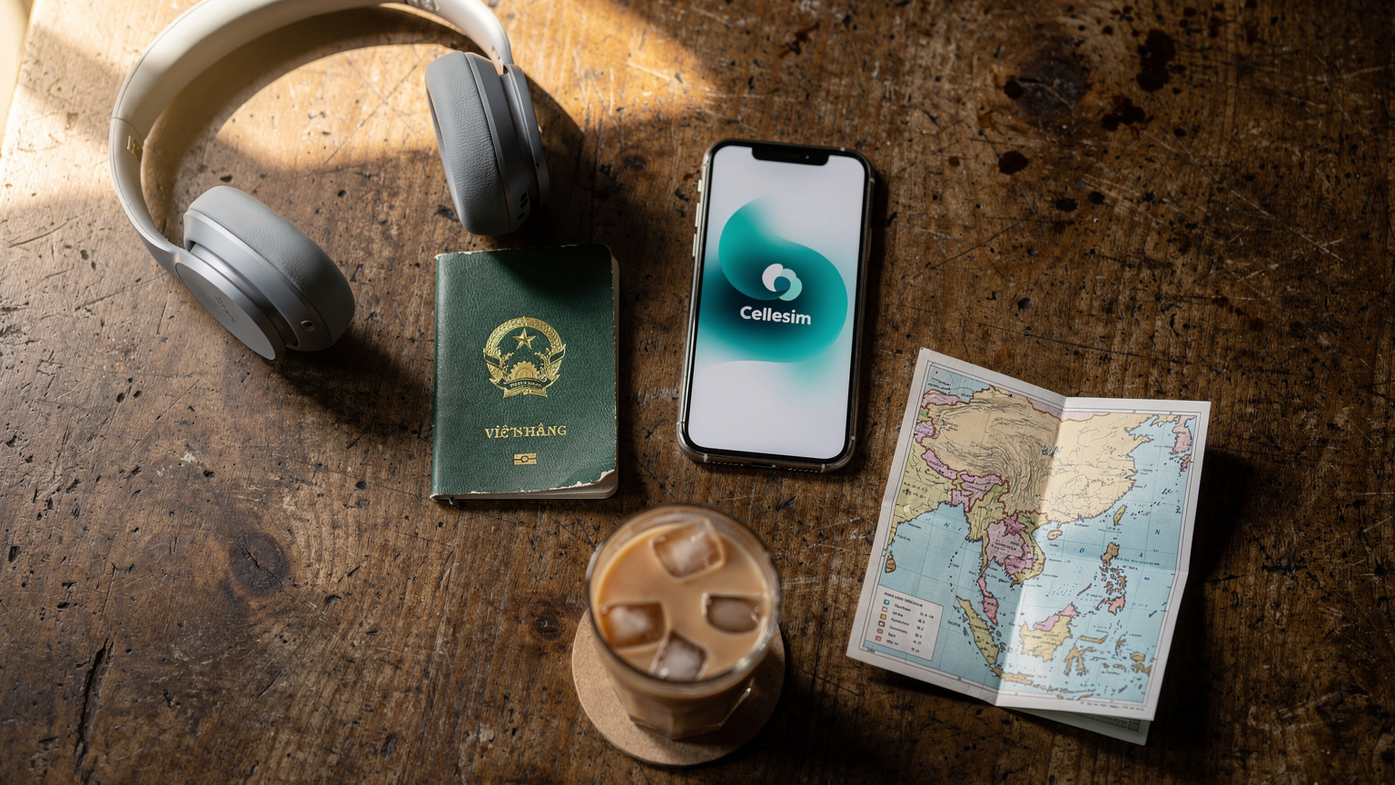 Một hộ chiếu Việt Nam, một điện thoại thông minh hiển thị logo Cellesim và một bản đồ Đông Nam Á được đặt gọn gàng trên bàn cà phê, tạo cảm giác về sự chuẩn bị cho chuyến đi.