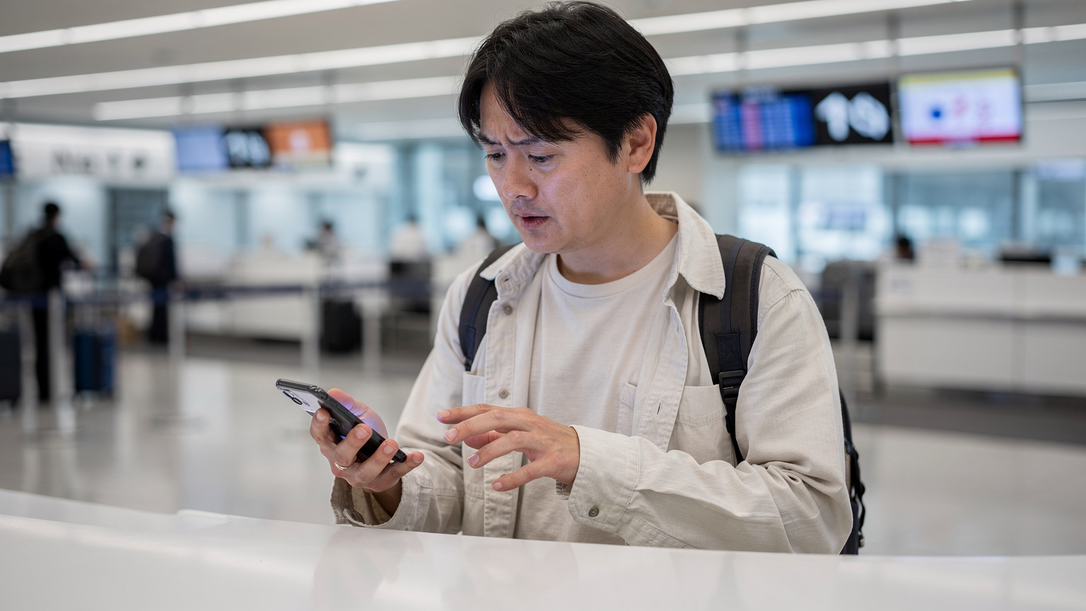 空港のチェックインカウンターで、スマートフォンのeSIM設定に悩む旅行者。画面にはエラーメッセージが表示されている。