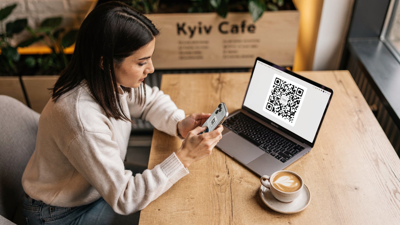 Жінка зосереджено сканує QR-код eSIM зі свого ноутбука за столиком у затишному кафе в Києві, готуючись до поїздки.