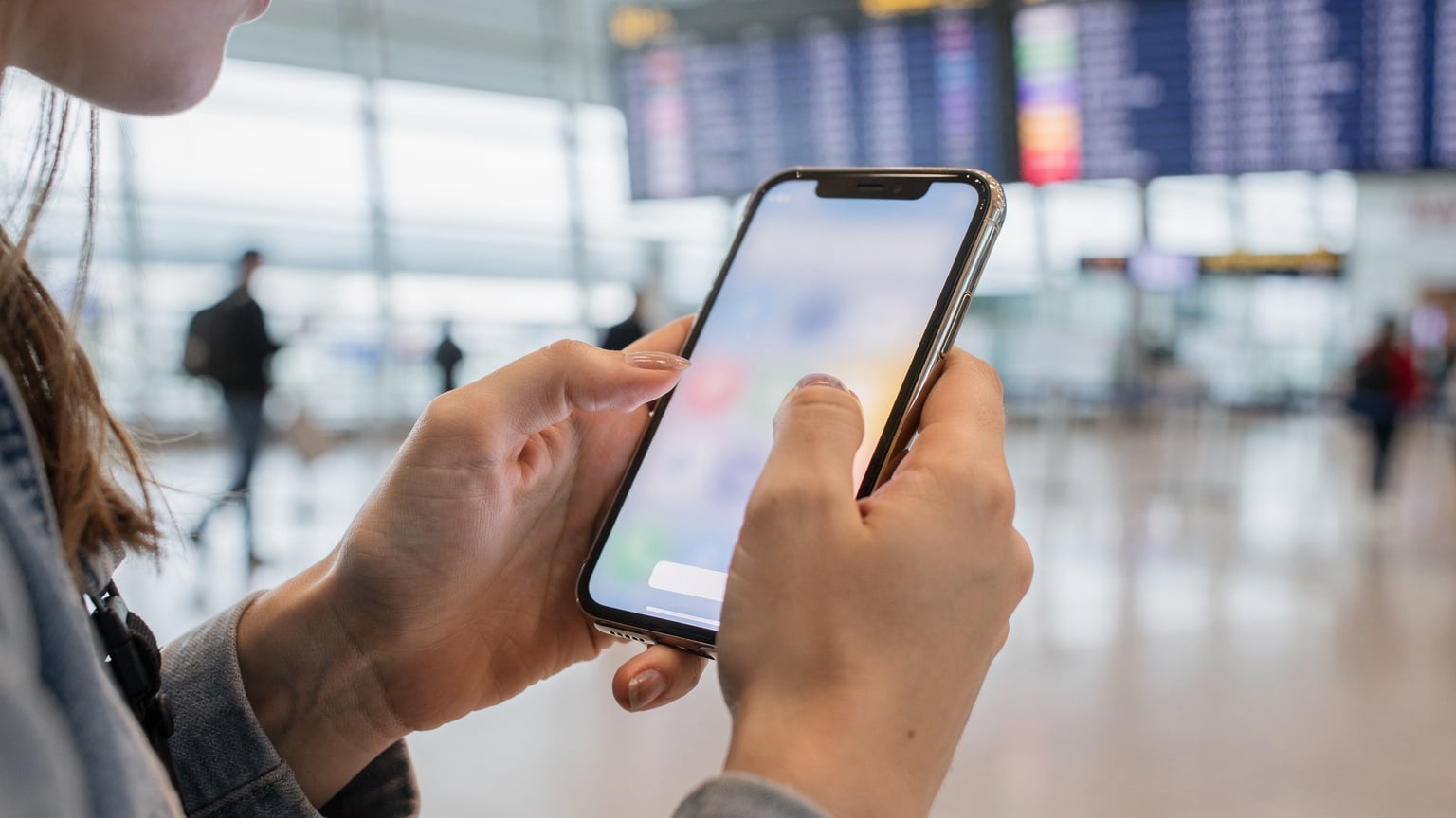 Zbliżenie na dłonie studentki trzymającej smartfon i skanującej kod QR w celu aktywacji eSIM, na tle rozmytego wnętrza lotniska Heathrow. Uwagę zwracają detale jej dłoni i telefonu.
