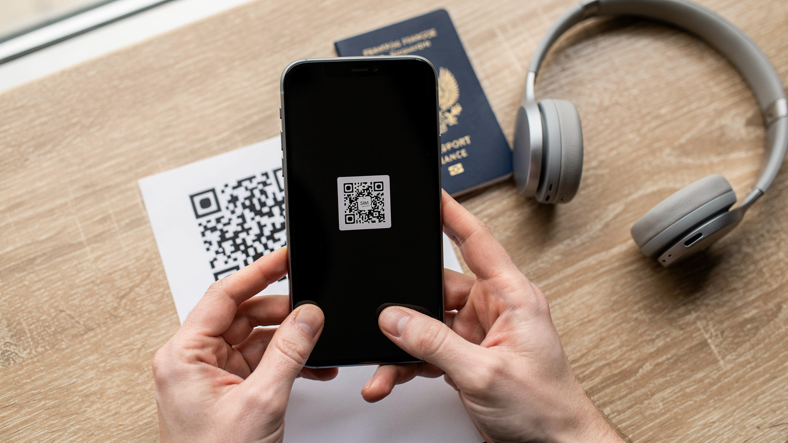 Gros plan sur des mains scannant un QR code eSIM avec un passeport français.