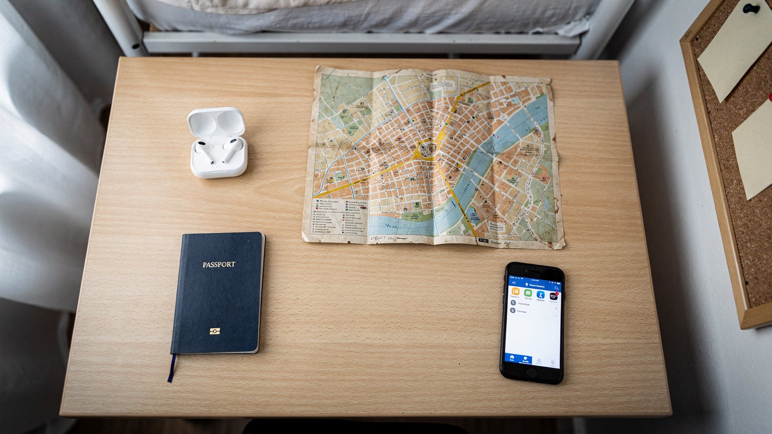 Bir hostel odasının masasında, pasaport, kulaklık, harita ve akıllı telefonun bulunduğu düzenli bir flat-lay fotoğrafı, gezginin planlama anını yansıtıyor.