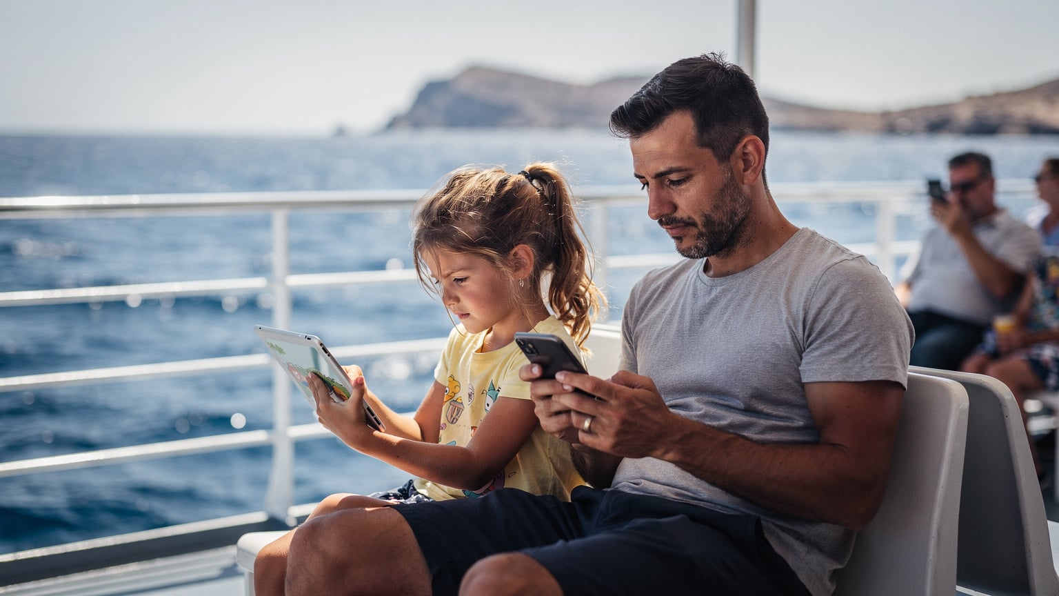 Yunan Adaları'nda bir feribotta, genç bir kız tabletinde çizgi film izlerken, diğer yandan babası telefonunda eSIM ayarlarını kontrol ediyor. Ege Denizi'nin mavi suları uzakta görünüyor.