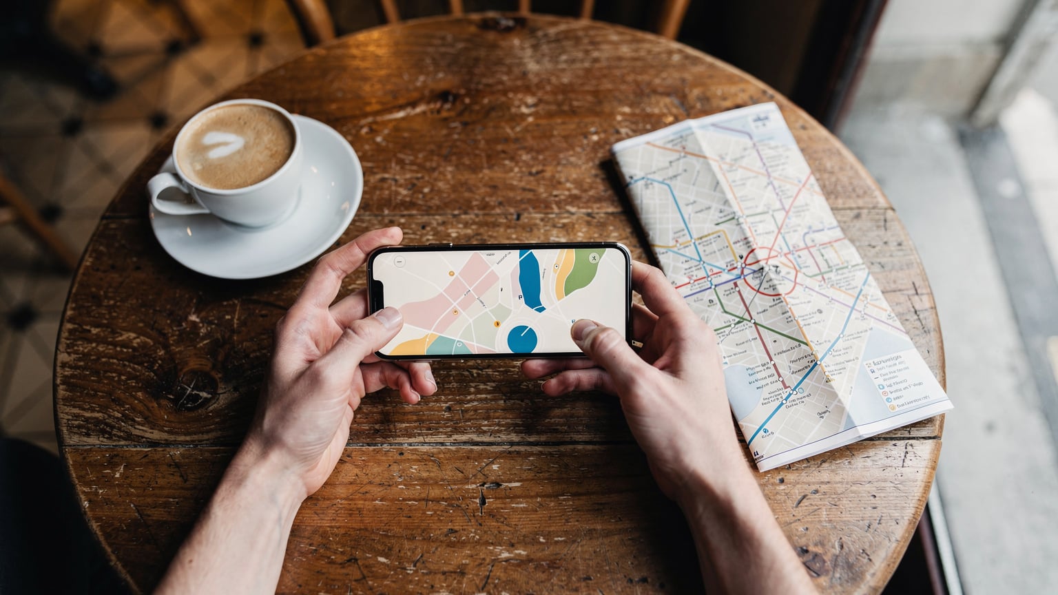 Bir kafe masasında, bir gezginin elinde akıllı telefon ve açık bir harita uygulaması, yanında bir fincan kahve ve Paris metro haritası görünüyor, telefon ekranında bir eSIM sağlayıcısının uygulama arayüzü kısmen seçilebiliyor.