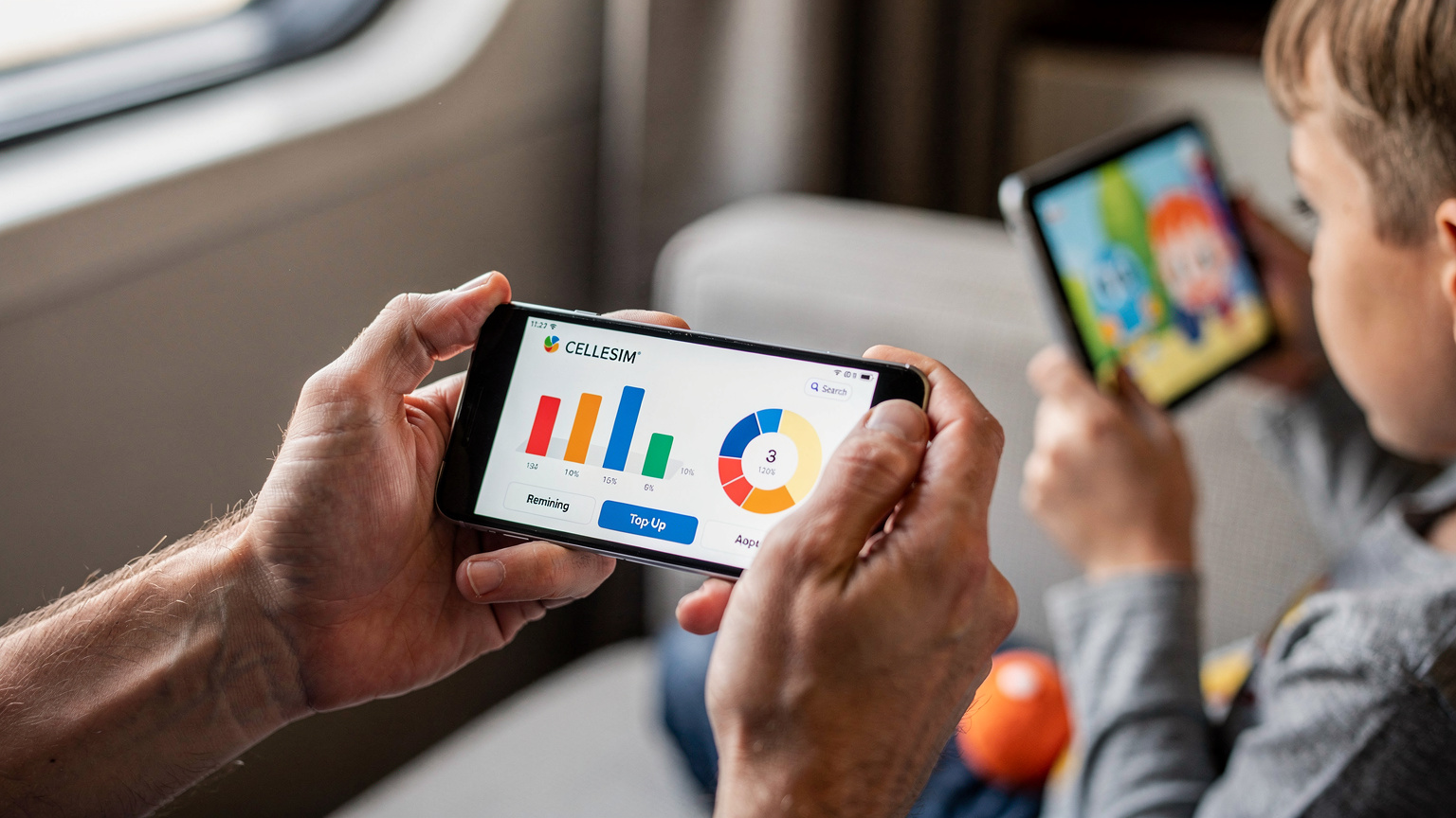 A close-up shot of a parent's hands holding a smartphone, actively interacting with the Cellesim app interface, showing a data usage dashboard. In the blurred background, a child's hand holds a tablet, watching a video, symbolizing data management for family entertainment.