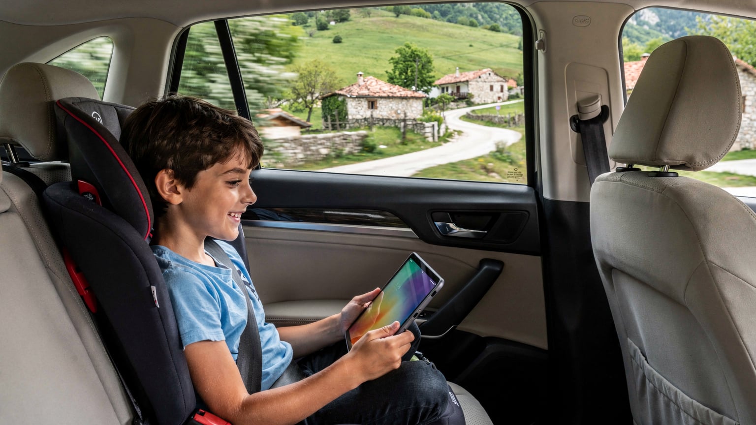 Ein Kind spielt begeistert auf einem Tablet im Rücksitz eines fahrenden Autos, während die Landschaft Albaniens im Hintergrund vorbeizieht. Das Tablet ist über einen mobilen Hotspot des Vaters verbunden.
