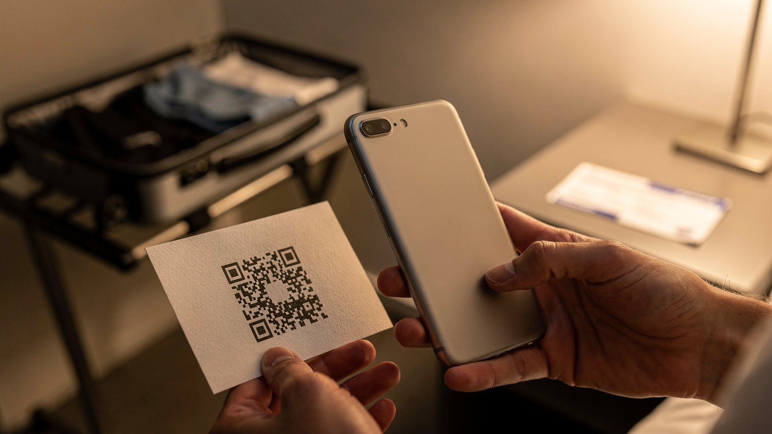En person skannar en QR-kod på en papperslapp med sin smartphone för att installera ett eSIM, med en resväska och boardingkort i bakgrunden på ett hotellrum.