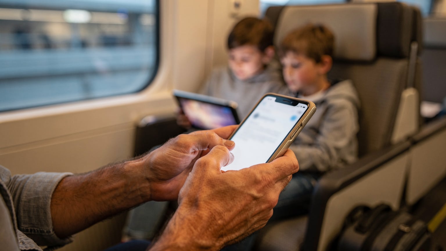 Un genitore configura l'hotspot del telefono per condividere la connessione con i dispositivi dei bambini, in un ambiente di viaggio, come un treno o un'area di sosta.