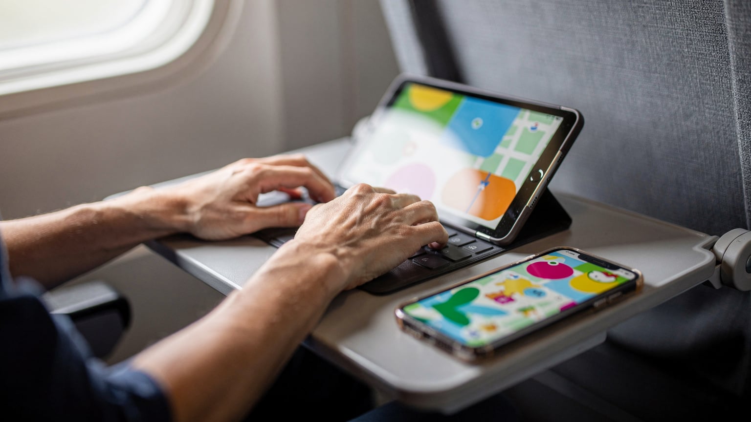 Mani di un adulto e di un bambino che interagiscono con un tablet e uno smartphone in un contesto di viaggio, con un'app di mappe e un gioco attivi.
