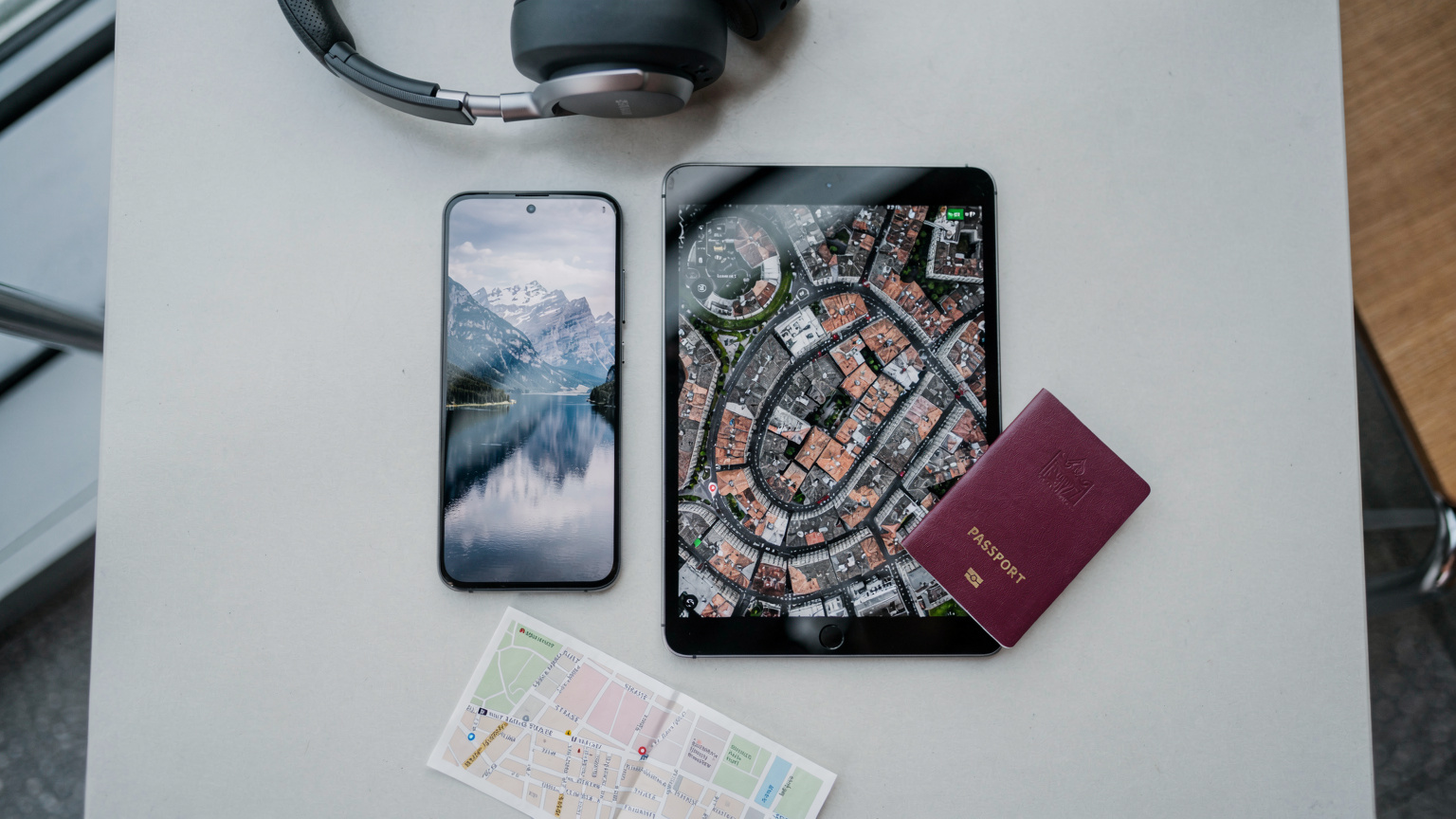 Un Samsung Galaxy S25 y un iPad con contenido descargado, junto a un pasaporte y auriculares en una mesa de café en un aeropuerto.