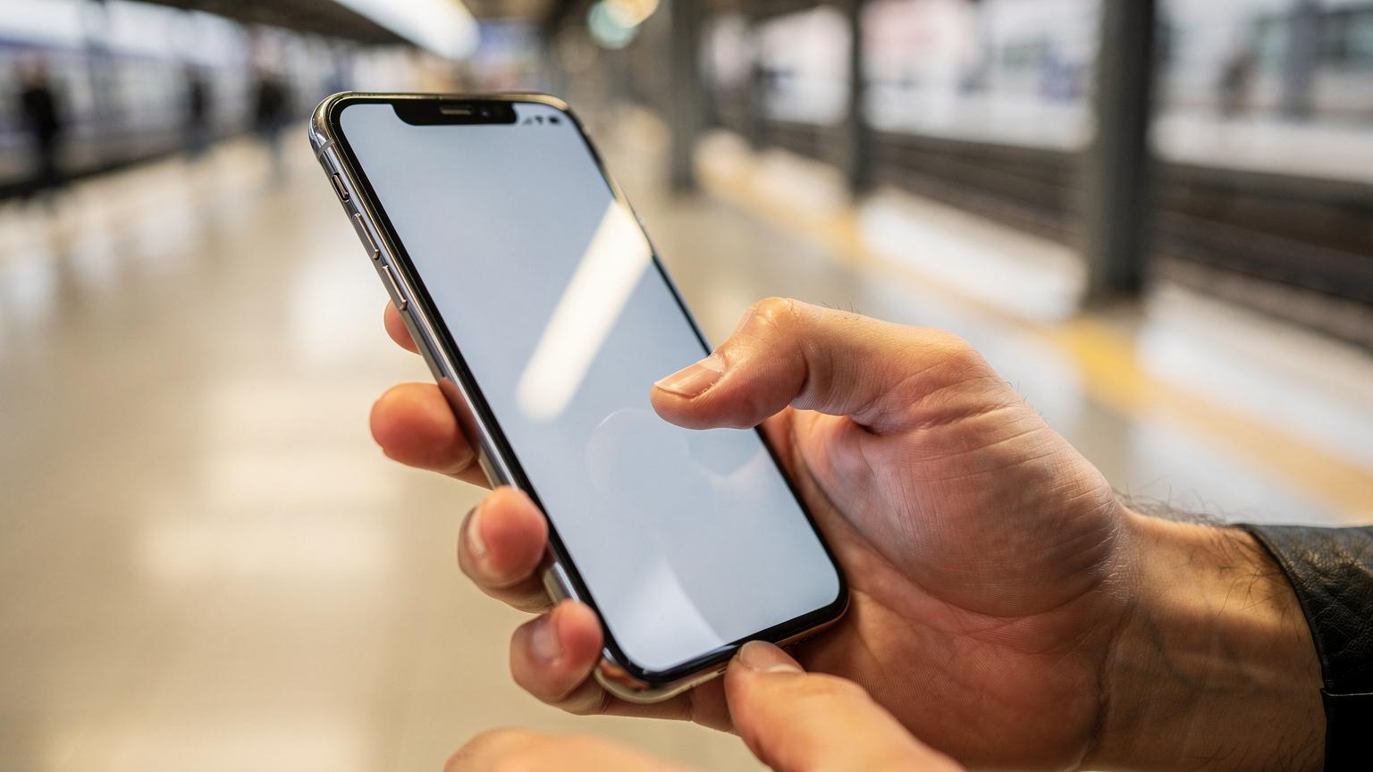 A close-up shot of human hands interacting with a smartphone, one finger tapping the screen to confirm an eSIM installation, with a blurred background of a brightly lit, modern train station platform in Spain.