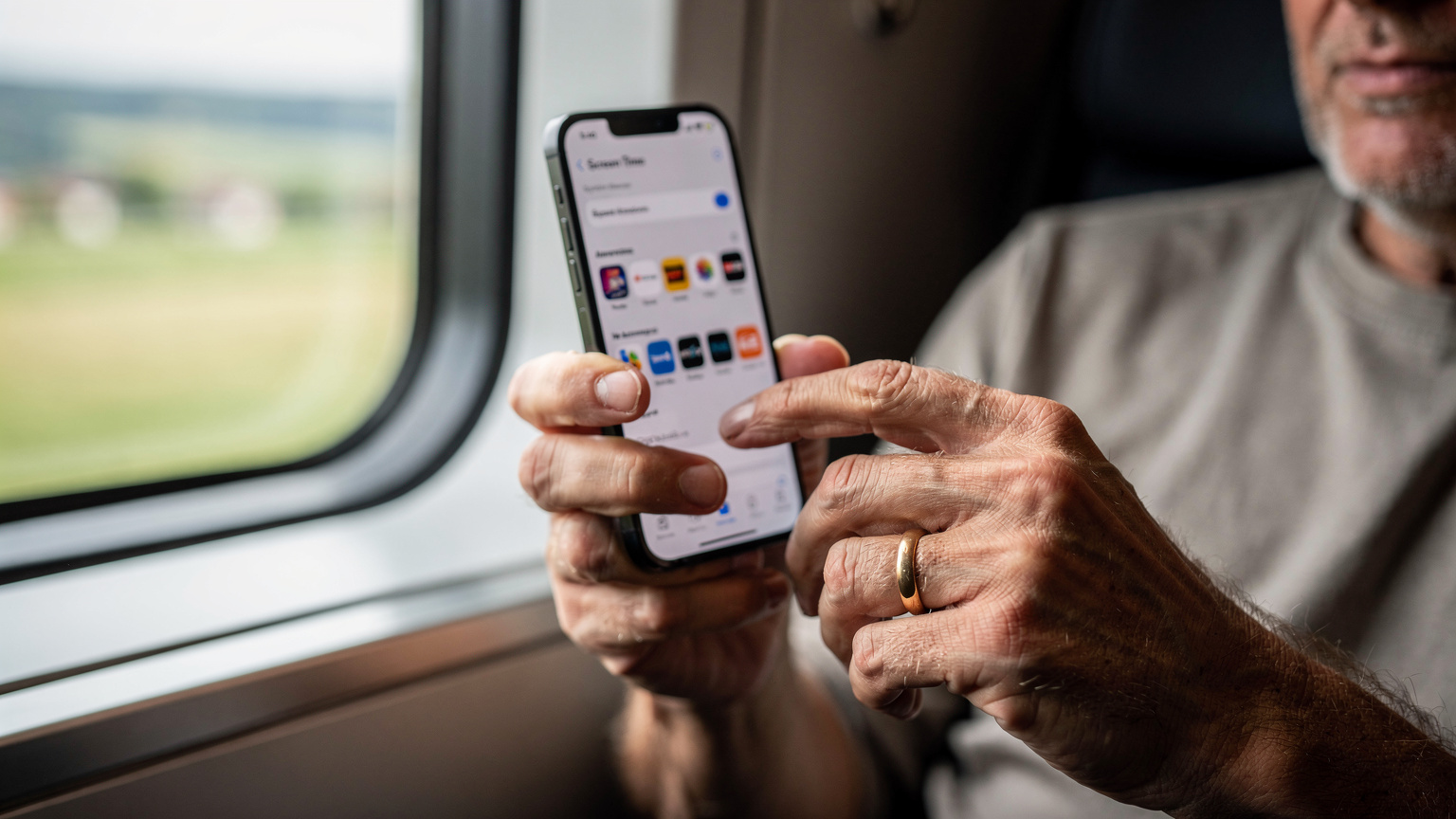 Manos de un padre configurando la función de "Tiempo de Uso" en un iPhone 14, con una lista de aplicaciones de streaming visibles, en el asiento de un tren de alta velocidad europeo.