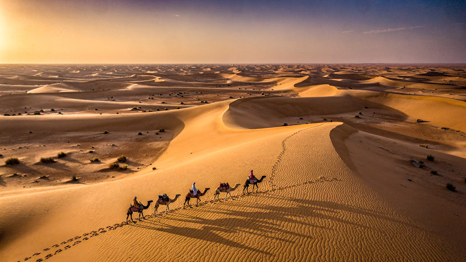 Fotografia z lotu ptaka przedstawiająca panoramiczny widok na wydmy pustyni Sahara w Maroku o zachodzie słońca, z karawaną wielbłądów w oddali, ukazując rozległość i piękno krajobrazu.