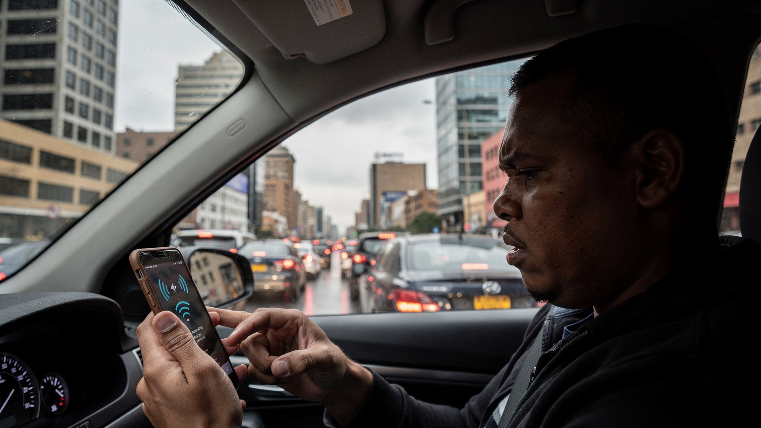 Een persoon kijkt gefrustreerd naar een smartphone met een 'geen service' melding, terwijl ze vastzitten in een trage file in het drukke centrum van Johannesburg, Zuid-Afrika.