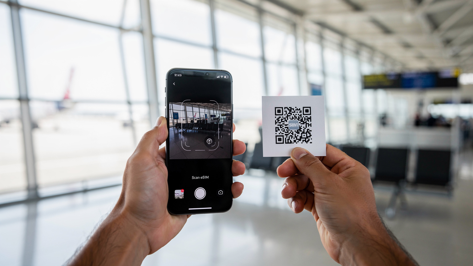 Un viajero activa su eSIM en un smartphone, escaneando un código QR con otra mano, en un ambiente de aeropuerto moderno y luminoso.