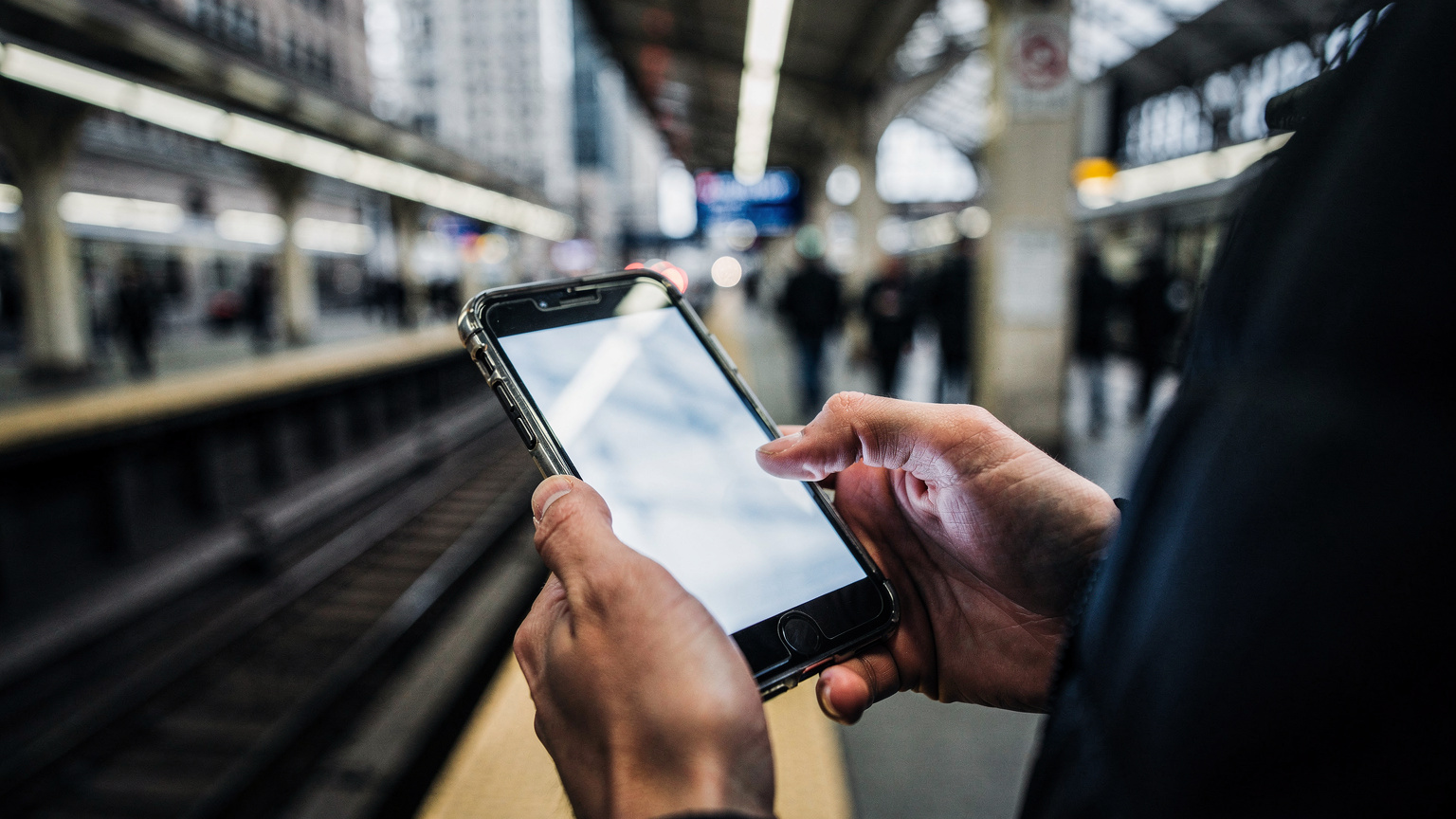 Detailní záběr rukou cestovatele, který na svém smartphonu prochází aplikaci pro veřejnou dopravu v Chicagu, s pozadím rušného vlakového nádraží.