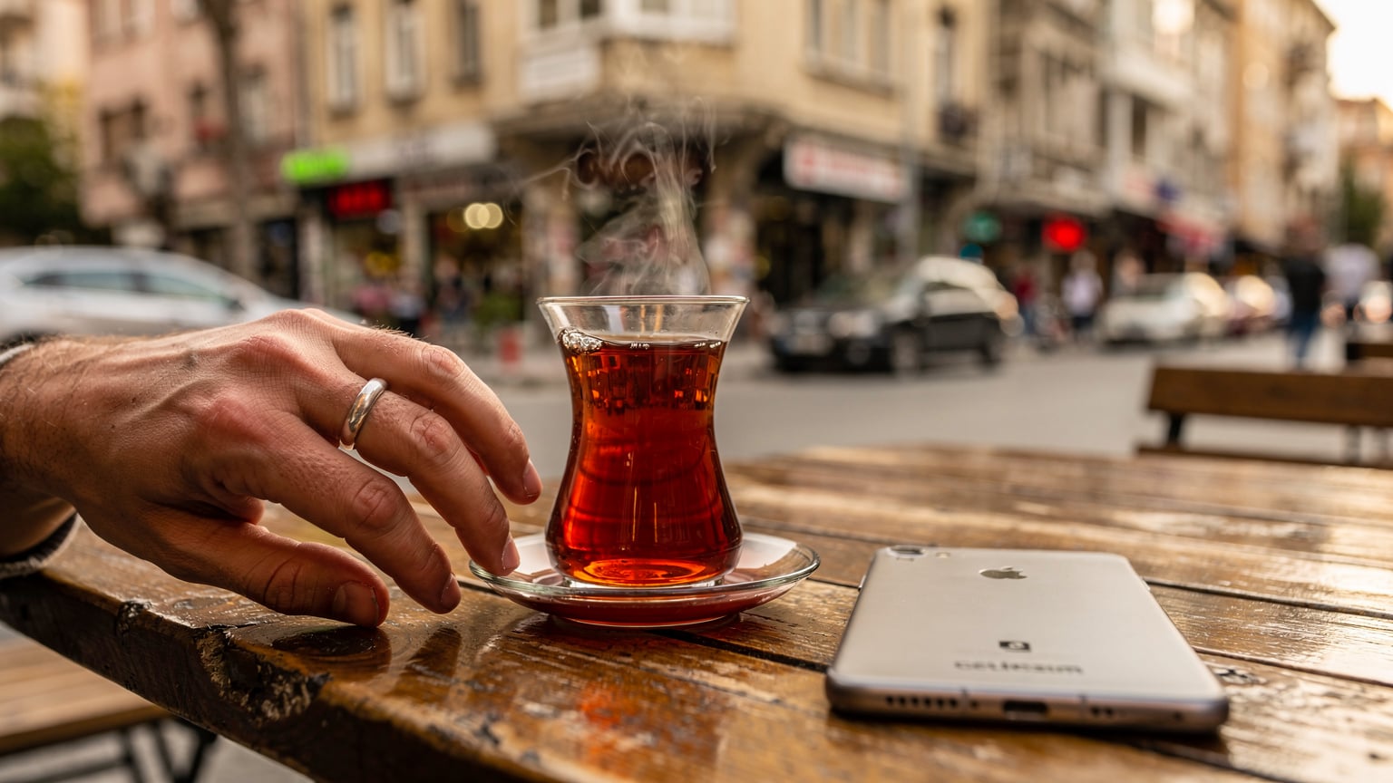 A person's hand reaches for a traditional Turkish tea glass on a small table at an outdoor cafe in Kadikoy, Istanbul, with a Cellesim-branded smartphone subtly placed on the table, indicating network presence.