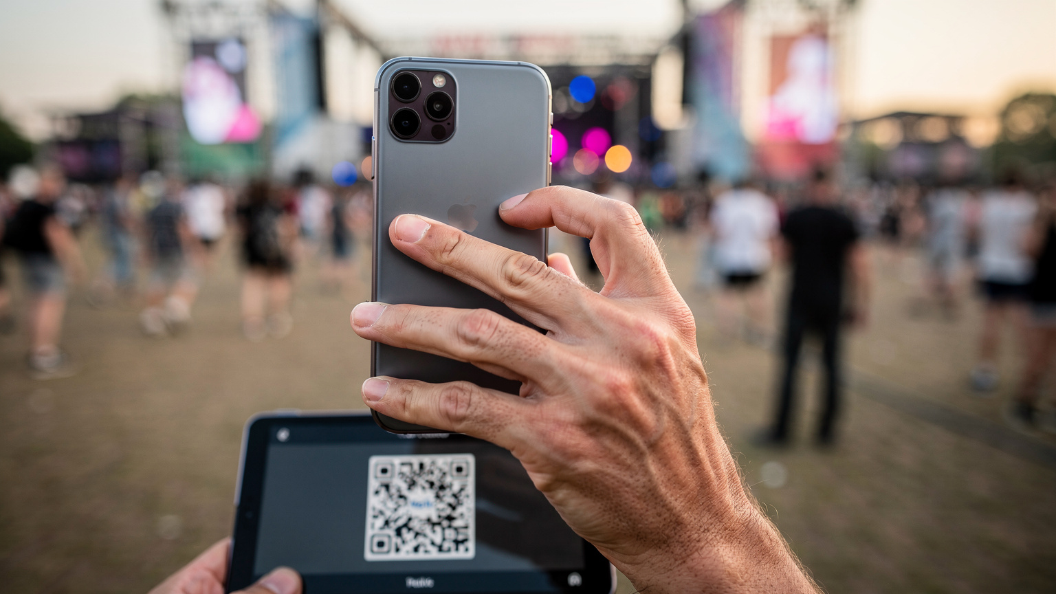 Eine Nahaufnahme zeigt Hände, die ein Smartphone halten, auf dem der QR-Code zur eSIM-Aktivierung auf einem anderen Bildschirm angezeigt wird, mit einem Hintergrund, der eine Menschenmenge andeutet.