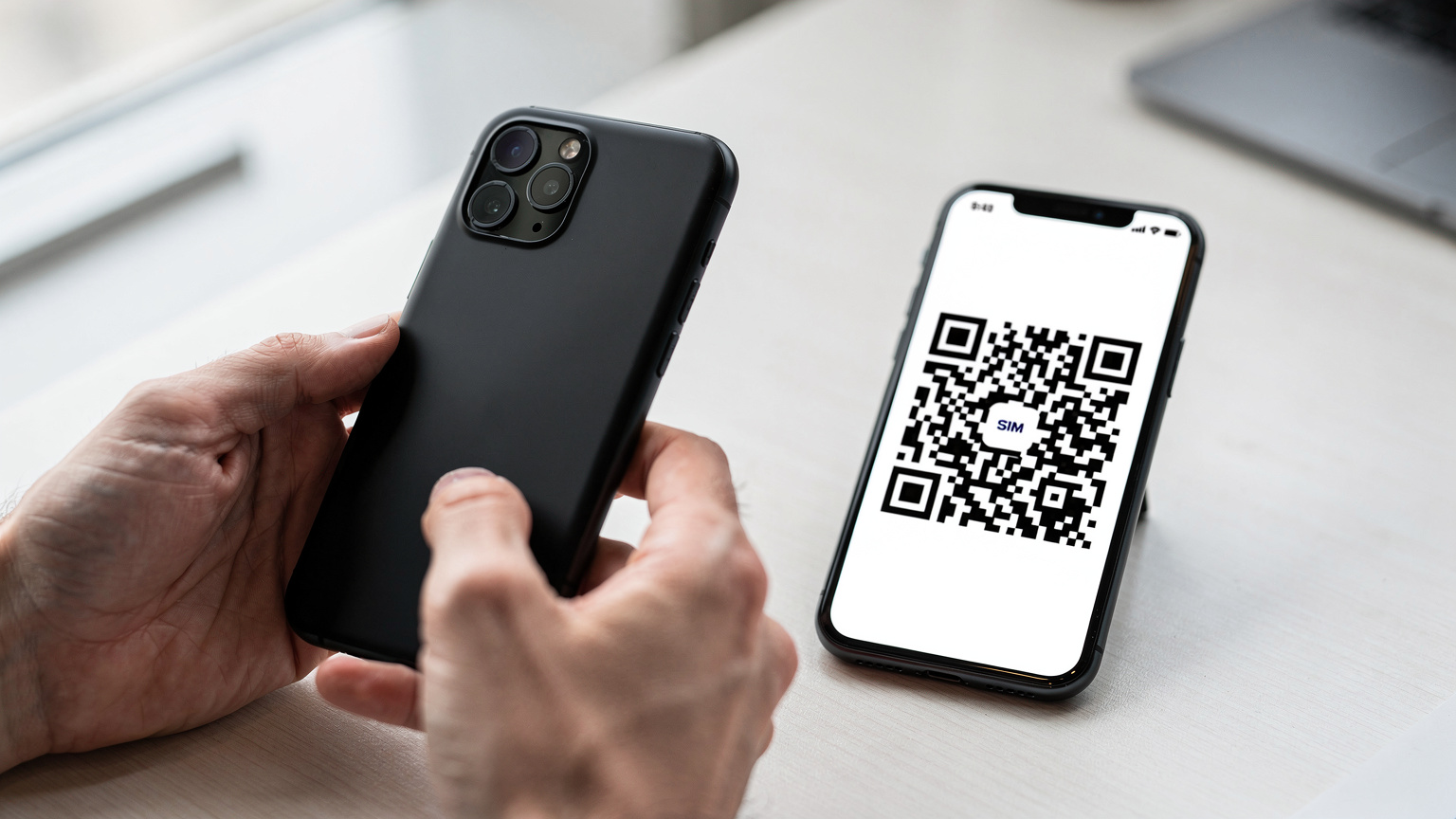 Un gros plan sur des mains tenant un smartphone affichant un QR code sur l'écran d'un autre appareil, symbolisant l'activation facile d'une eSIM avant un voyage.