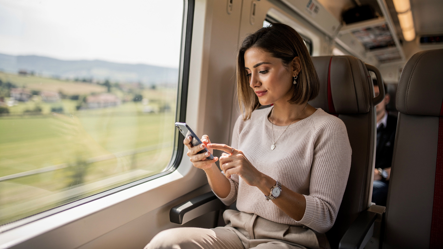 Una mujer joven en un tren de alta velocidad italiano, utilizando su teléfono para consultar mapas, mostrando la fluidez de la conectividad en movimiento.