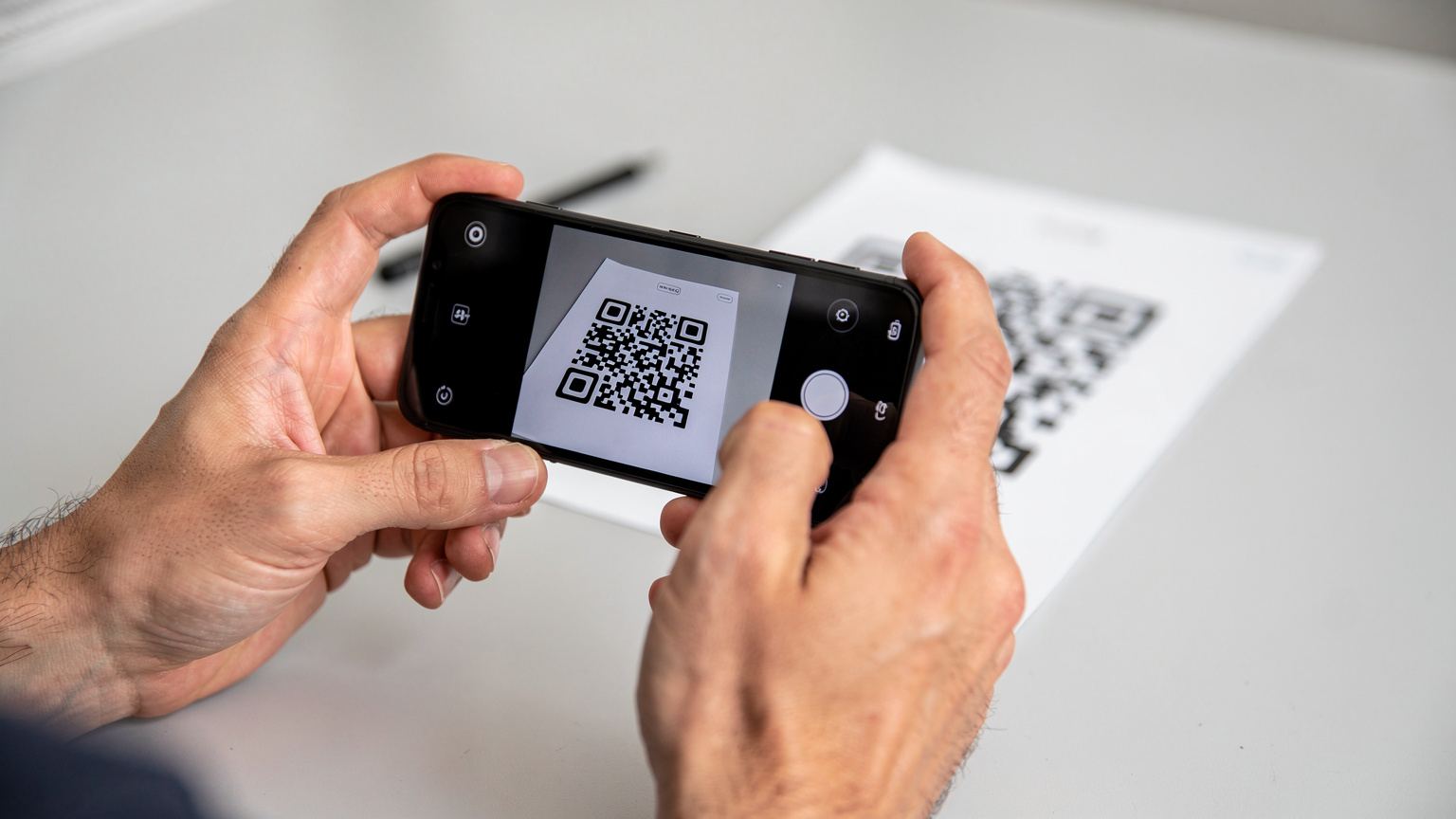 Nahaufnahme von zwei Händen, die ein Smartphone halten und einen QR-Code auf einem anderen Bildschirm oder einem ausgedruckten Blatt Papier scannen, um eine eSIM zu installieren.