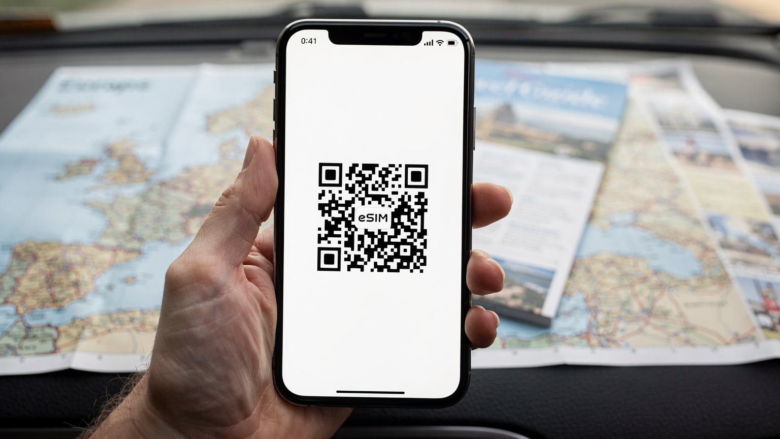 En hand håller en smartphone som visar en QR-kod för eSIM-aktivering, med en europeisk vägkarta synlig i bakgrunden.