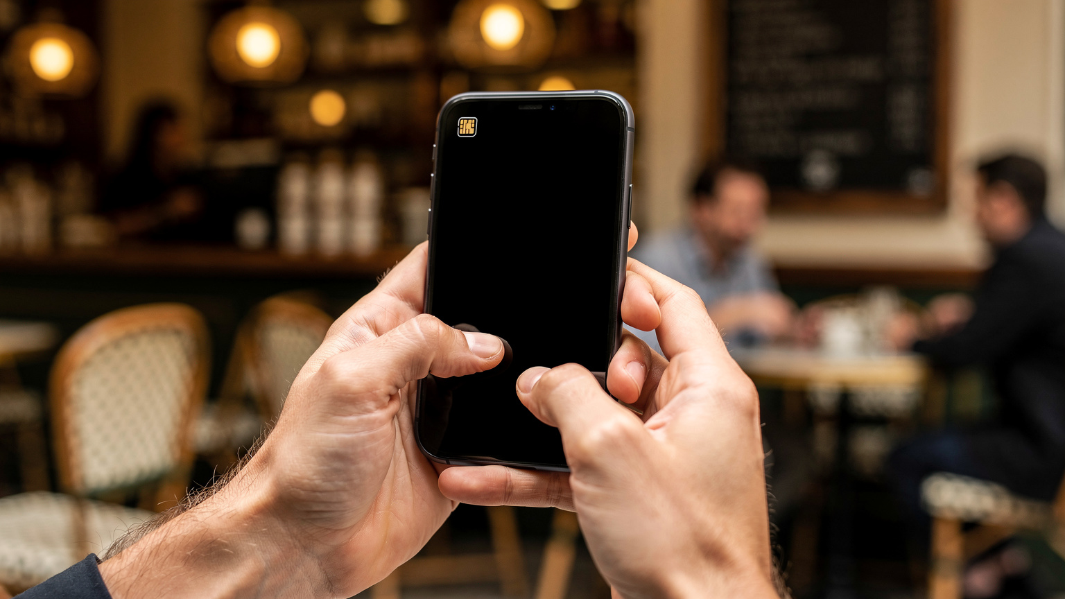 Крупний план рук, що тримають смартфон з активованим eSIM на фоні розмитого паризького кафе.