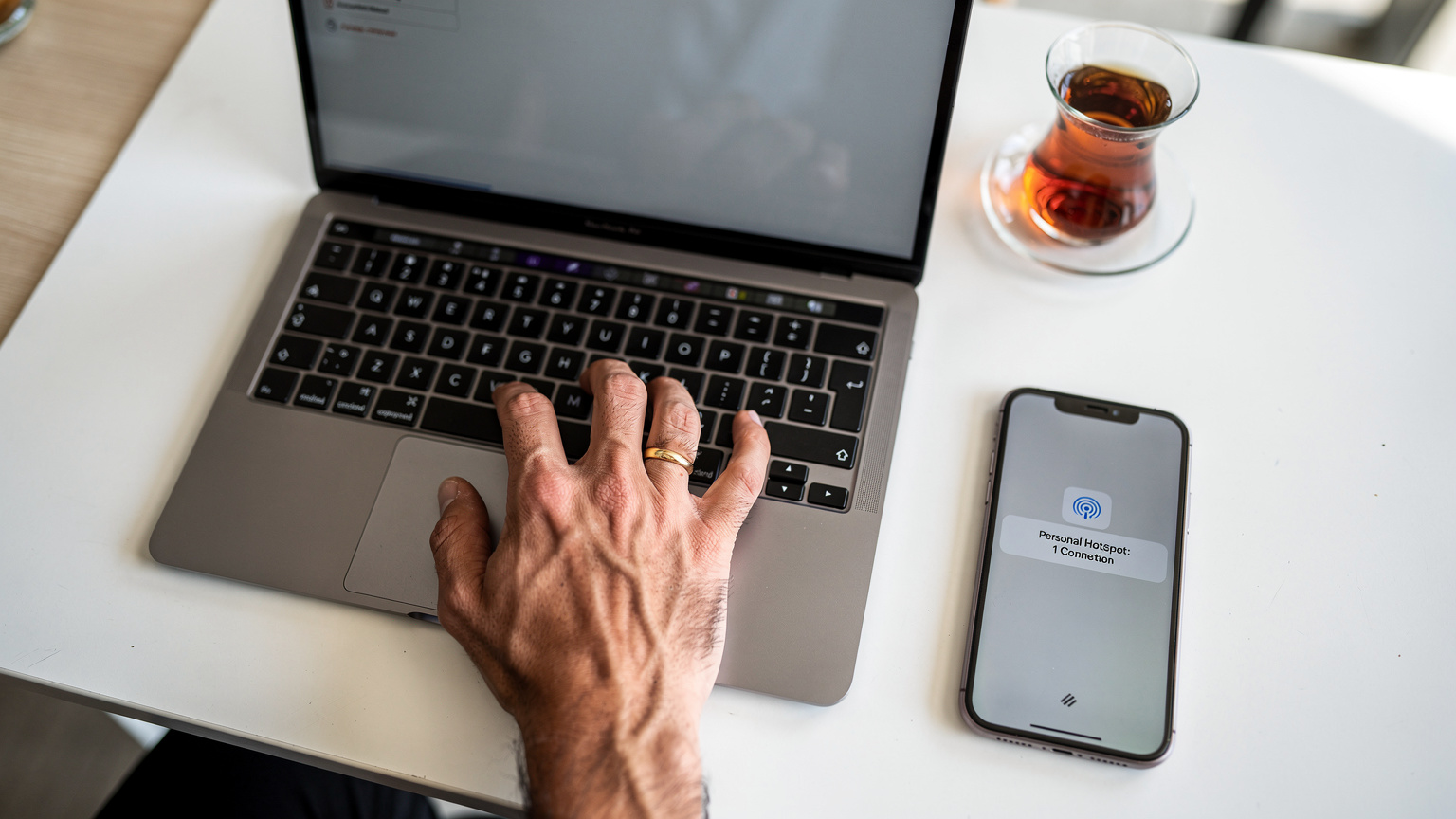 Bir el, MacBook Air M3'ün klavyesinde çalışırken, hemen yanında duran iPhone'dan mobil erişim noktasının aktif olduğunu gösteren bir bildirim ekranı beliriyor.