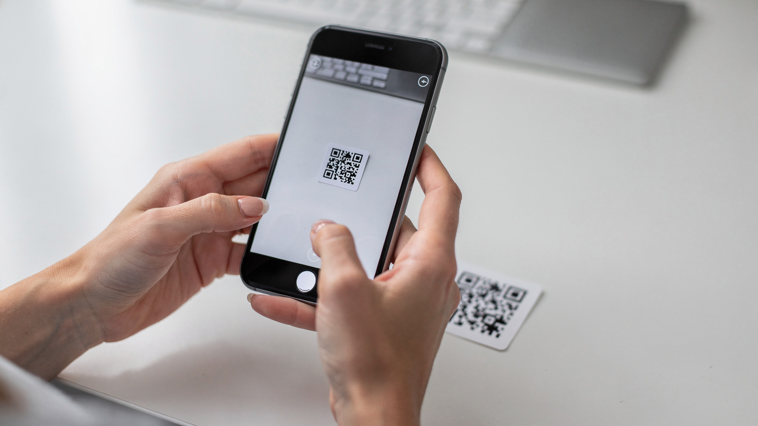 Bir kadının elleri, akıllı telefonunda eSIM kurulumu için bir QR kodunu taramak üzere kamerayı tutarken, arka planda bulanık bir QR kodu görünüyor.