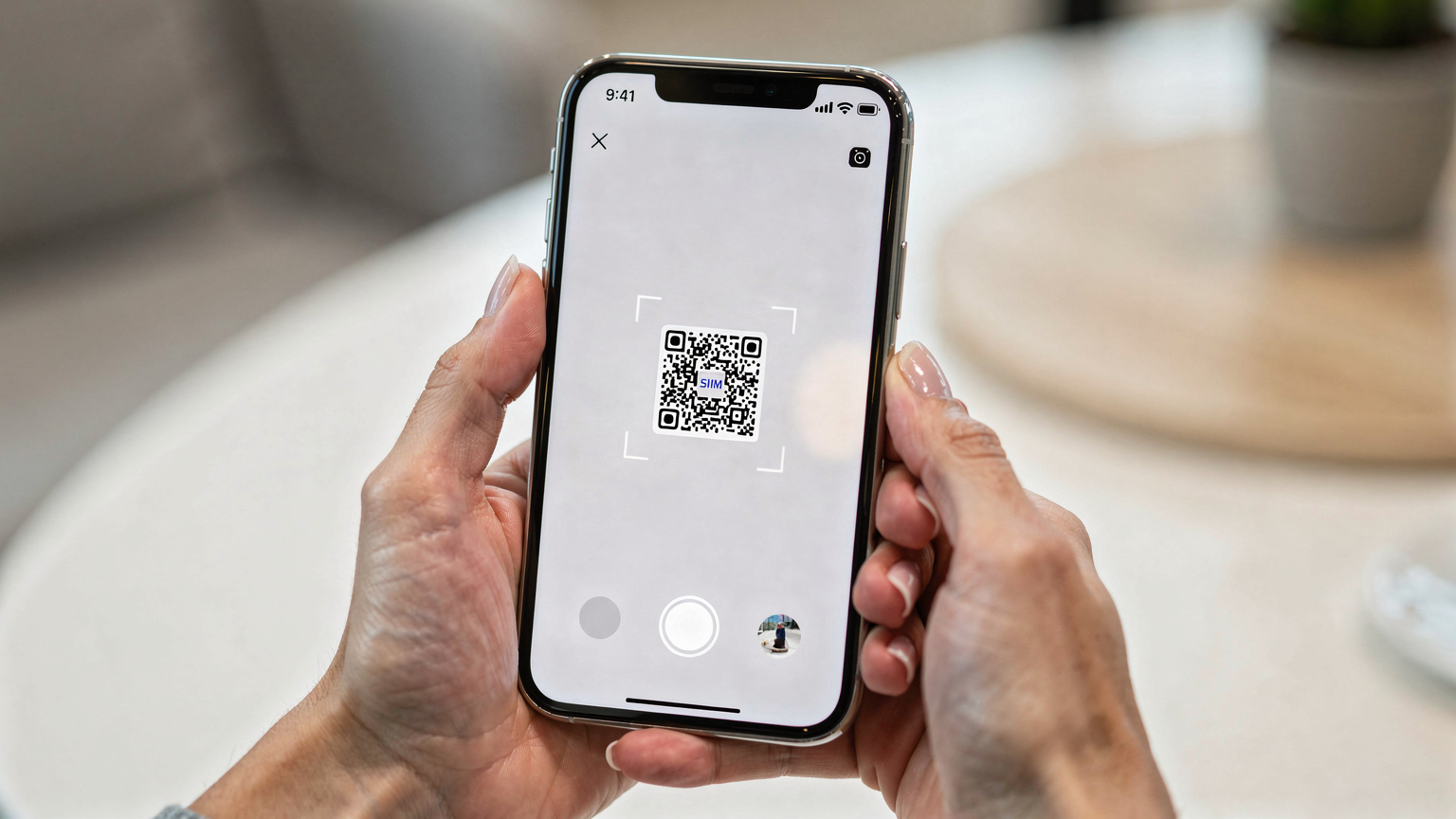Unas manos de adulto sostienen un iPhone 17, mientras la pantalla muestra el proceso de escaneo de un código QR para activar una eSIM. El fondo está ligeramente desenfocado, sugiriendo un ambiente de hogar o aeropuerto.