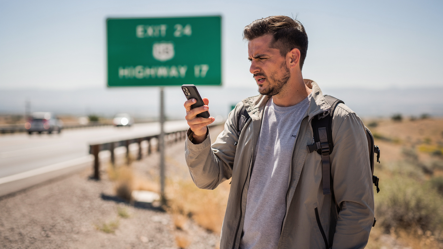 Un viaggiatore guarda il suo smartphone con un'espressione di frustrazione, mentre il segnale di rete è assente, sullo sfondo di un cartello stradale generico degli Stati Uniti.